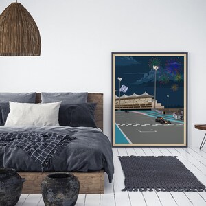 K&ouml;nnte beinhalten: Ein gerahmtes Poster mit einer n&auml;chtlichen Illustration einer Rennstrecke mit einer karierten Flagge und Feuerwerk im Hintergrund. Das Poster h&auml;ngt an einer wei&szlig;en Wand &uuml;ber einem grauen Bett mit einem Holz-Kopfteil.