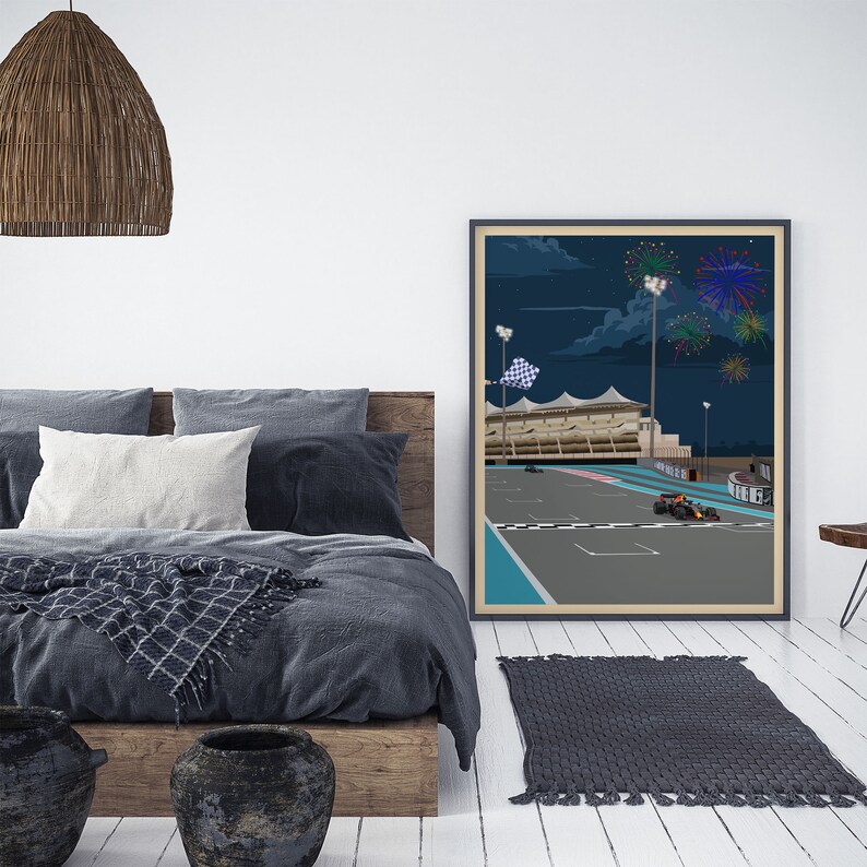 K&ouml;nnte beinhalten: Ein gerahmtes Poster mit einer n&auml;chtlichen Illustration einer Rennstrecke mit einer karierten Flagge und Feuerwerk im Hintergrund. Das Poster h&auml;ngt an einer wei&szlig;en Wand &uuml;ber einem grauen Bett mit einem Holz-Kopfteil.