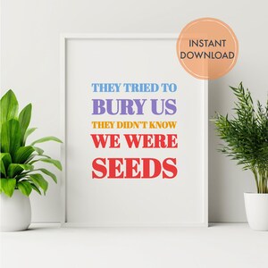 May include: A framed print with the text "THEY TRIED TO BURY US THEY DIDN'T KNOW WE WERE SEEDS" in blue, purple, orange, and red. The print is in a white frame and has a circular "INSTANT DOWNLOAD" sticker. Potted plants flank the print.