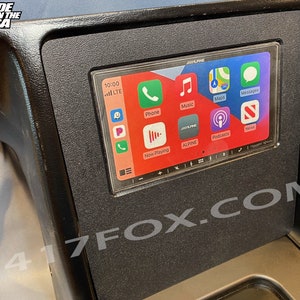 May include: A black car dashboard console with a built-in Alpine touchscreen display. The screen shows the Apple CarPlay interface with app icons for Phone, Music, Maps, and Podcasts. The text "MADE IN THE USA" and "417FOX.COM" are visible.