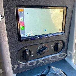 May include: A black car dashboard with a Pioneer touchscreen car stereo displaying a Google Maps navigation screen. The stereo has a blue backlight and the screen shows a map with a blue arrow pointing north. The dashboard also has a black knob for the air conditioning and a black switch for the vent.