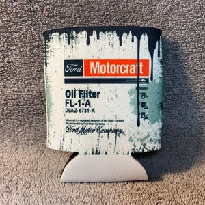 May include: A white and green can cooler with a black border. The can cooler has a Ford Motorcraft logo and the text "Oil Filter FL-1-A D9AZ-6731-A Ford Motor Company".