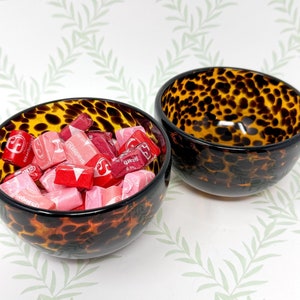 May include: Two decorative glass bowls with a tortoise shell pattern. One bowl is filled with pink and red Starburst candies. The bowls have a glossy finish and are set against a white background with a leaf pattern.