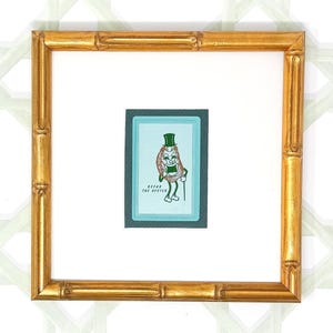 May include: A gold-colored picture frame with a white mat and a cartoon illustration of a green-hatted oyster character. The illustration is titled "Oscar the Oyster".