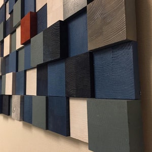 May include: A wall art piece made of wooden squares in various shades of blue, gray, white, and red. The squares are arranged in a staggered pattern, creating a modern and abstract design.