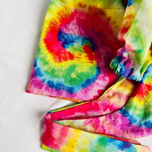 May include: A colourful tie-dye fabric headband with a rainbow swirl pattern. The headband is made of a soft, stretchy material and has a gathered elastic band.
