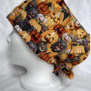Puede incluir: Un gorro de quirófano con un estampado de Halloween con caras de calabaza naranja, negra y blanca.