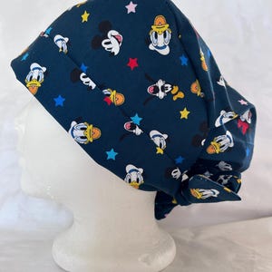 May include: A dark teal surgical scrub cap with a pattern of Mickey Mouse, Donald Duck, and other cartoon characters, plus stars in various colours. The cap is tied at the back.