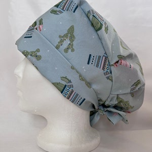 Puede incluir: Un gorro de quirófano azul claro con estampado de cactus. El gorro tiene un lazo en la parte posterior.