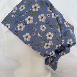 Puede incluir: Un gorro de quirófano azul con un estampado floral blanco. El gorro tiene un lazo en la parte posterior.