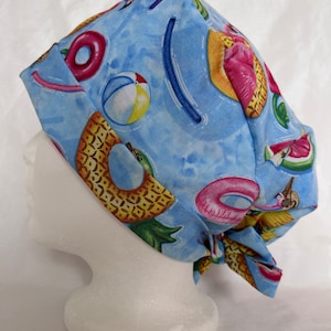 May include: A blue scrub hat with a summer-themed print featuring pineapples, watermelon, and inflatable pool toys.