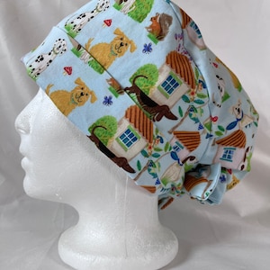 Könnte beinhalten: Eine hellblaue OP-Mütze mit einem Muster aus Hunden, Häusern und anderen Tieren. Die Mütze ist auf einem weißen Mannequin-Kopf gebunden.