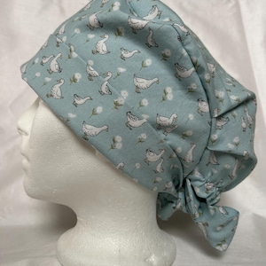 Peut inclure: Une charlotte chirurgicale bleu clair ornée d'un motif répétitif d'oies blanches et de petites fleurs blanches ressemblant à des pissenlits. Le bonnet présente un bandeau avant replié et une fermeture à nouer à l'arrière en tissu mat.