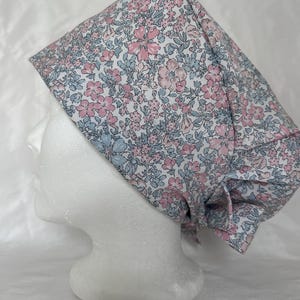 Peut inclure: Un bonnet de travail blanc avec un motif floral rose et bleu. Le bonnet a une attache à l'arrière.