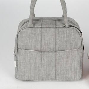 Puede incluir: Una bolsa de almuerzo gris con cierre de cremallera y asa superior. La bolsa tiene un peque&ntilde;o bolsillo en la parte delantera con la palabra "CAMINO" impresa en &eacute;l.