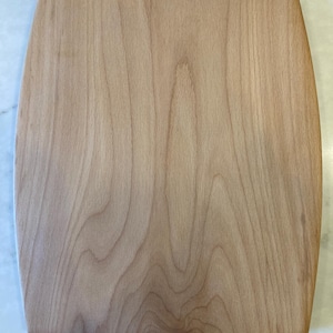 以下が含まれることがあります： 角が丸い長方形の木製まな板。明るい色の木材で作られており、自然な木目模様が特徴です。表面は滑らかで、未完成のようです。