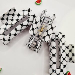 Op de afbeelding: Drie haarclips met een wit en zwart patroon met een geometrisch ontwerp. De clips zijn open en dicht, waarbij het interne veermechanisme te zien is. Verspreid liggen decoratieve watermeloenstukjes.