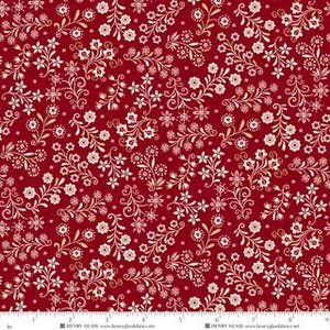 May include: A deep red fabric featuring a repeating pattern of cream-colored floral sprigs, delicate leaves, and swirling vines. A white measuring tape is visible at the bottom edge, showing a length of nine inches across the fabric surface.