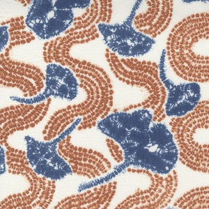 May include: A white fabric with a repeating pattern of blue and brown abstract shapes. The shapes are made up of small dots and resemble stylized flowers.