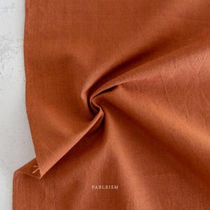 May include: A close-up of a rust-colored fabric with a subtle cross-hatch pattern. The fabric is soft and has a slightly textured surface. The text "FABLEISM" is visible in the lower right corner of the image.