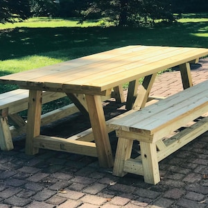 May include: A wooden picnic table with two matching benches. The table has a light-colored wood finish and a classic A-frame leg design. The benches are the same color and style as the table. The table is approximately 72 inches long.