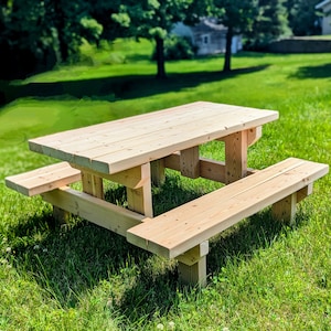 May include: A wooden picnic table with two benches. The table and benches are made of unfinished wood and are sitting on a grassy lawn.