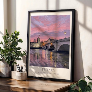 May include: A framed art print featuring a painting of Putney Bridge in London at sunset with a pink and purple sky, stone arches, and water reflections. The print includes the text PUTNEY WANDSWORTH LONDON in a clean, centered font at the bottom.