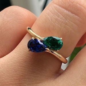 Pode incluir: Um anel de ouro com uma gema azul e verde em forma de pêra.
