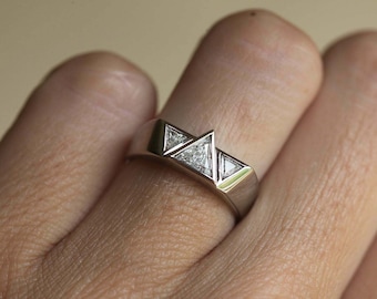 Pode incluir: Um anel de banda de prata com três diamantes triangulares engastados no centro.