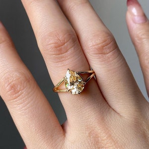 Puede incluir: Un anillo de oro con una piedra preciosa de forma de pera de color champán engastada en un diseño de caña dividida.