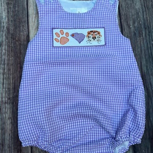 May include: A purple and white gingham baby onesie with a paw print, heart, and tiger embroidered on the front.