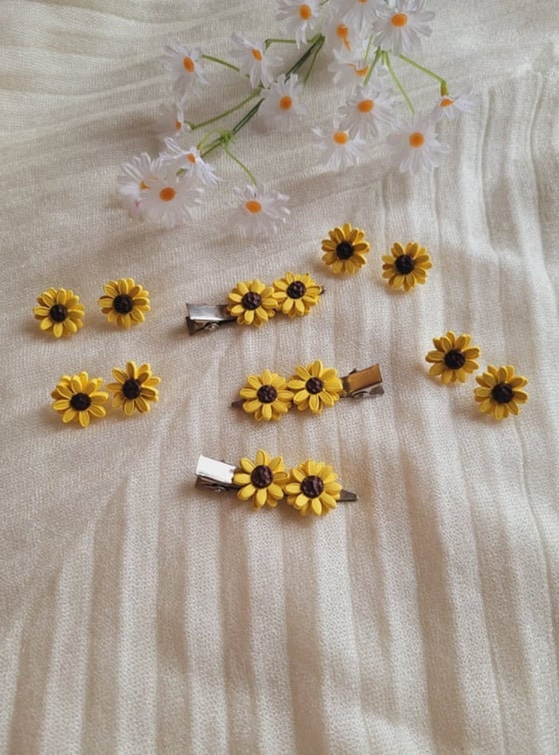 May include: A set of sunflower hair clips. There are three clips with three sunflowers each and four individual sunflower clips. The clips are silver and the sunflowers are yellow with brown centers.