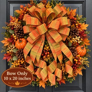 May include: A decorative wreath featuring orange and green striped fabric ribbon, artificial autumn leaves, pinecones, and small berries. A brown oval sign at the bottom displays the text: Bow Only 10 x 20 inches, with a small maple leaf icon.