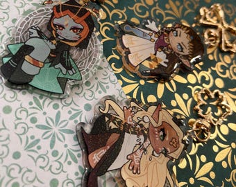 May include: Three character charms featuring anime-style characters. The charms are made of clear acrylic with glitter accents. The characters are a green and black creature with red eyes, a white and gold character with brown hair and a brown and gold character with blonde hair.