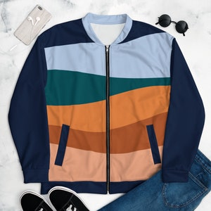 May include: A bomber jacket featuring a front panel with horizontal wavy stripes in light blue, teal, orange, brown, and peach. The jacket has solid dark navy blue sleeves, a matching navy blue hem and collar, and a central silver-toned zipper closure.