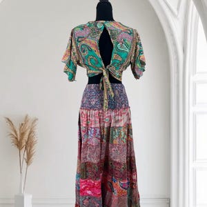 May include: A two-piece bohemian outfit featuring a paisley print crop top with a keyhole back and a long patchwork skirt. The top is green, pink, and gold, and the skirt is a mix of pink, purple, and red fabrics.