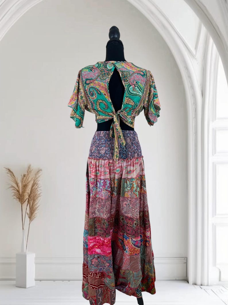 May include: A two-piece bohemian outfit featuring a paisley print crop top with a keyhole back and a long patchwork skirt. The top is green, pink, and gold, and the skirt is a mix of pink, purple, and red fabrics.