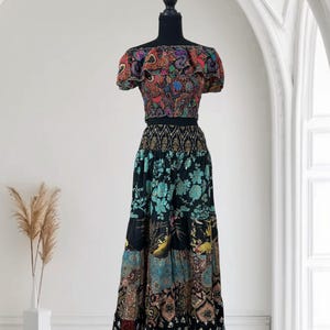 May include: A two-piece bohemian outfit on a mannequin. The top is a multicolored, off-the-shoulder crop top with a ruffled neckline. The skirt is a long, patchwork design in black, teal, and brown with floral and geometric patterns.