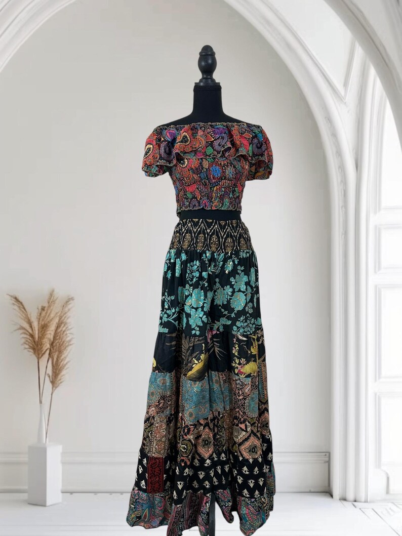 May include: A two-piece bohemian outfit on a mannequin. The top is a multicolored, off-the-shoulder crop top with a ruffled neckline. The skirt is a long, patchwork design in black, teal, and brown with floral and geometric patterns.