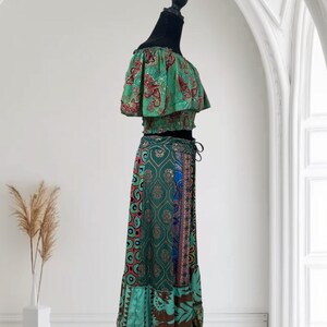 May include: A two-piece outfit on a black mannequin. The top is off-the-shoulder with a green and red paisley pattern. The skirt is a long, flowing style with a mix of patterns in green, blue, and brown. The skirt has a drawstring waist.
