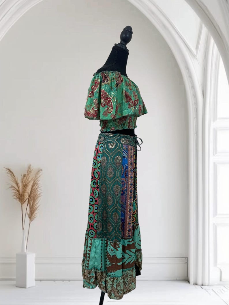 May include: A two-piece outfit on a black mannequin. The top is off-the-shoulder with a green and red paisley pattern. The skirt is a long, flowing style with a mix of patterns in green, blue, and brown. The skirt has a drawstring waist.