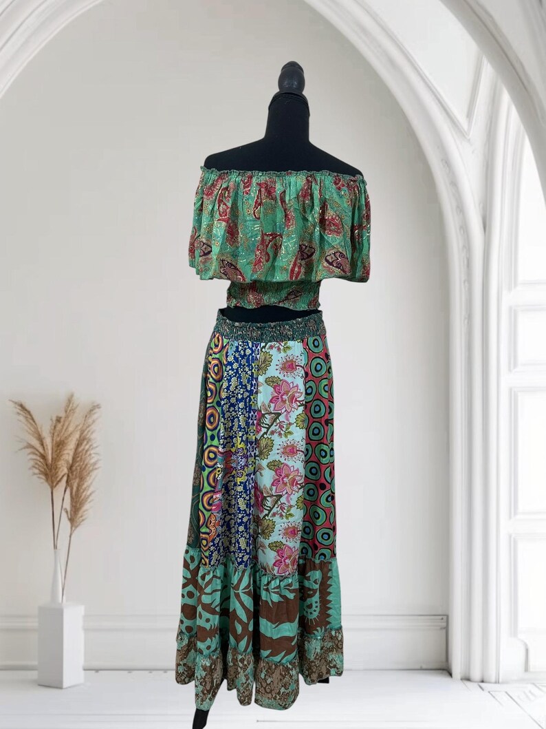 May include: A two-piece bohemian outfit on a mannequin. The off-the-shoulder crop top is green with a red and gold paisley pattern. The long skirt is a patchwork of floral and geometric patterns in shades of blue, green, and brown.