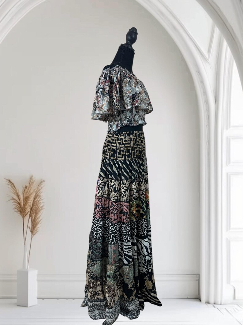 May include: A two-piece outfit on a mannequin. The top is a ruffled, off-the-shoulder style with a floral pattern in shades of blue, green, and red. The skirt is a patchwork design with various patterns and colors, including black, white, pink, and green.
