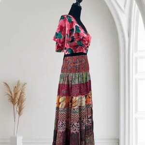May include: A two-piece outfit on a black mannequin. The top is a pink floral print with short sleeves and a V-neck. The skirt is a patchwork design in various colors, including red, orange, and purple. The skirt is floor-length.
