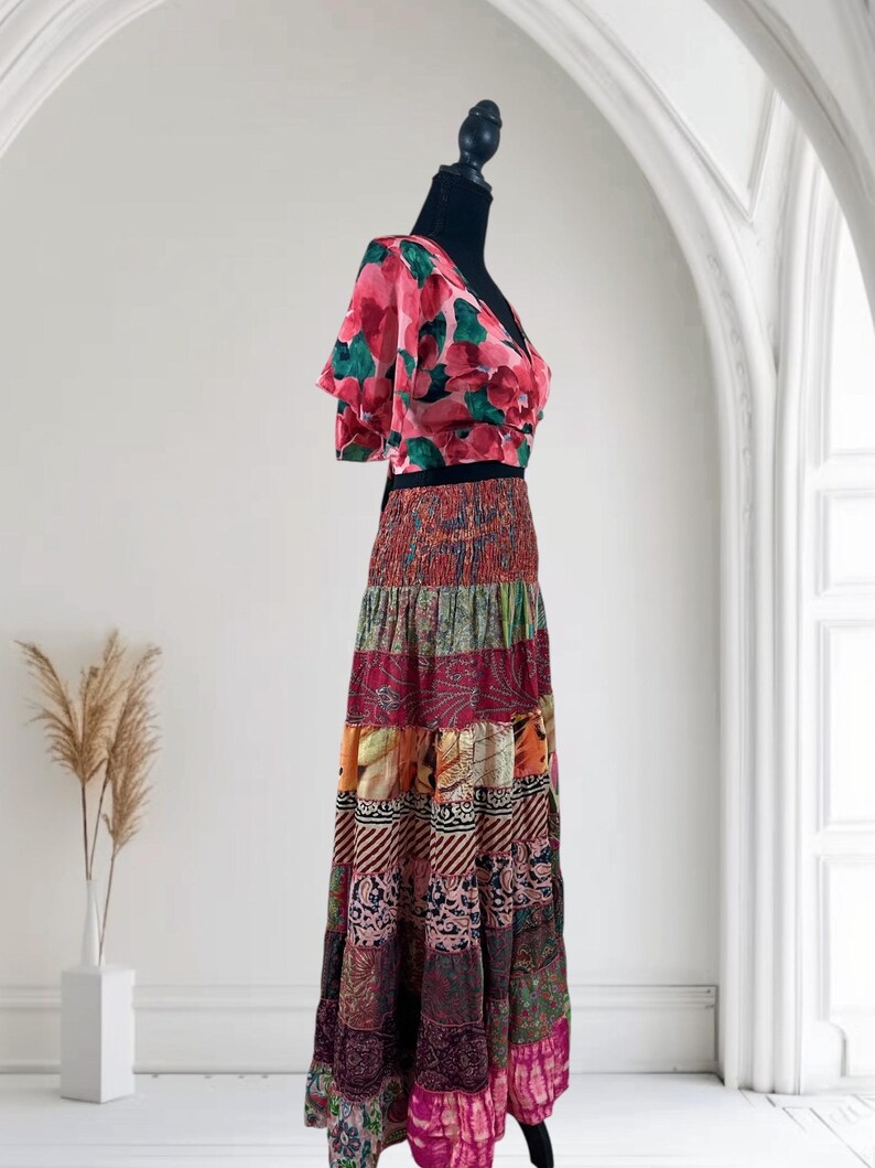 May include: A two-piece outfit on a black mannequin. The top is a pink floral print with short sleeves and a V-neck. The skirt is a patchwork design in various colors, including red, orange, and purple. The skirt is floor-length.