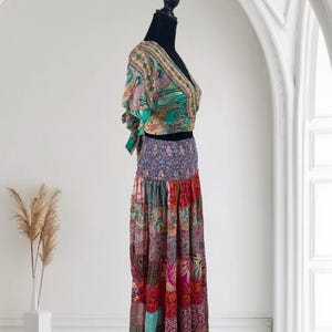 May include: A two-piece bohemian outfit on a black mannequin. The top is a wrap-style crop top with a V-neck and short sleeves, featuring a paisley print in green, pink, and gold. The skirt is a patchwork design in various colors and patterns.