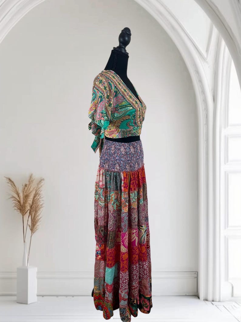 May include: A two-piece bohemian outfit on a black mannequin. The top is a wrap-style crop top with a V-neck and short sleeves, featuring a paisley print in green, pink, and gold. The skirt is a patchwork design in various colors and patterns.