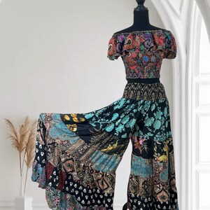 May include: A two-piece bohemian outfit on a mannequin. The off-the-shoulder crop top and wide-leg pants feature a patchwork design with floral and paisley patterns in shades of black, blue, red, and gold. The outfit is displayed against a white background.