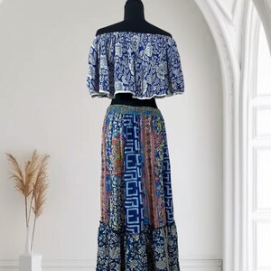 May include: A two-piece bohemian outfit on a mannequin. The off-the-shoulder top is blue with a white floral pattern. The long skirt features a patchwork design with various patterns and colors, including blue, pink, and orange. The skirt has a ruffled hem.