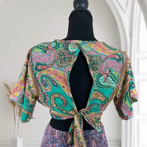 May include: A colorful paisley print top with a keyhole back and tie closure. The top features shades of teal, pink, yellow, and green. The bottom portion of the outfit is a multi-colored skirt with a ruffled design.